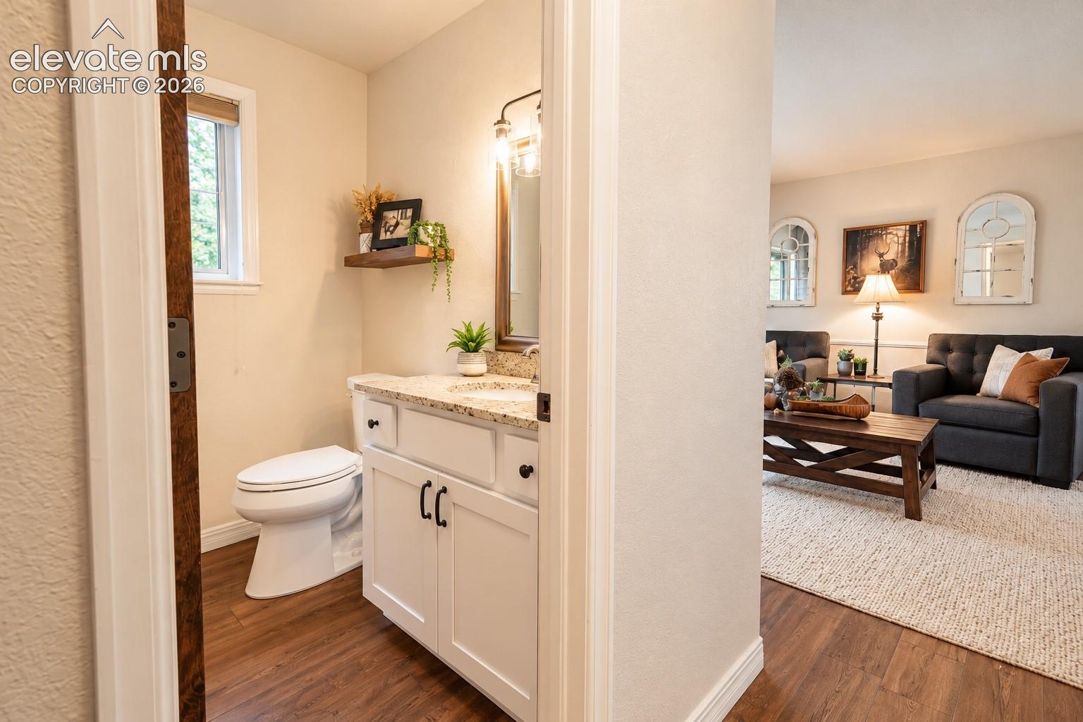 Powder room featuring a white vanity with granite-finish countertop, wood-finish flooring, and a window