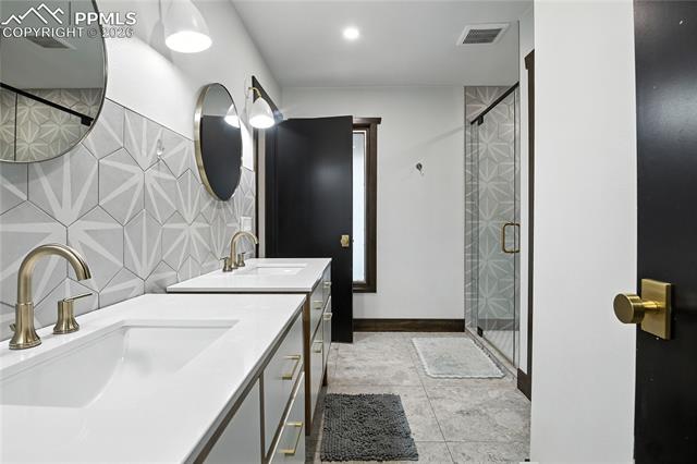 Full bathroom featuring a stall shower, backsplash, two vanities, and light tile patterned floors