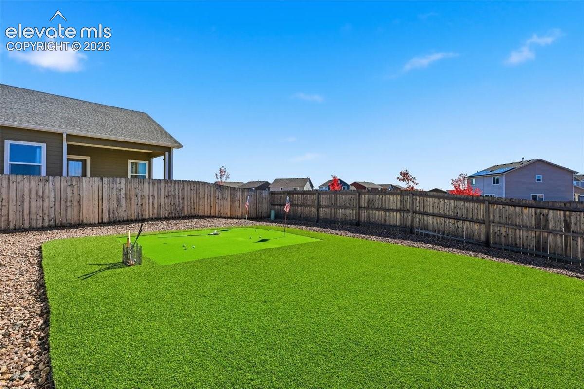 Rear yard featuring artificial turf, integrated putting green, and a perimeter wood privacy fence