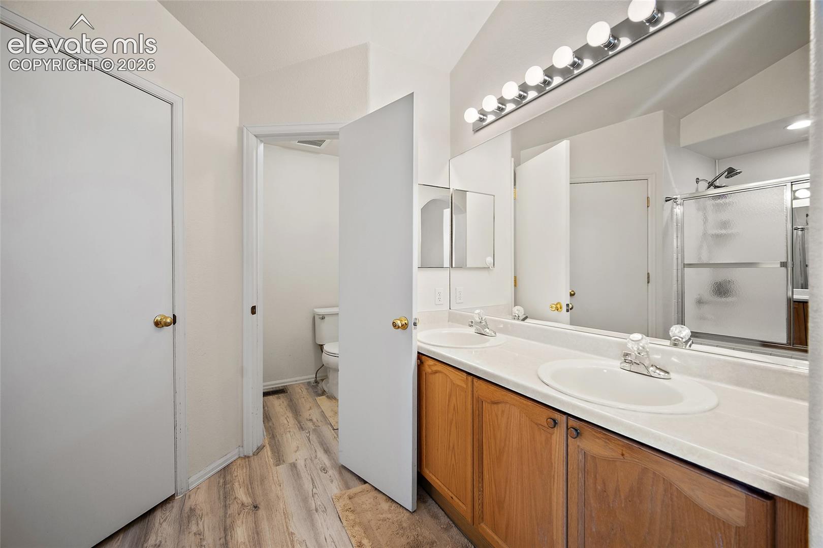 Bathroom featuring a double vanity with wood-finish cabinetry, dual undermount sinks, and a full-width mirror with overhead bar lighting