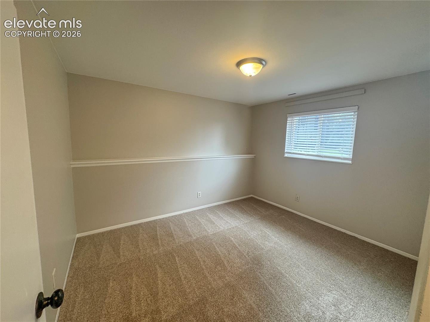 Neutral-toned interior room featuring wall-to-wall carpeting, horizontal window blinds, a decorative chair rail, and a flush-mount ceiling light fixture