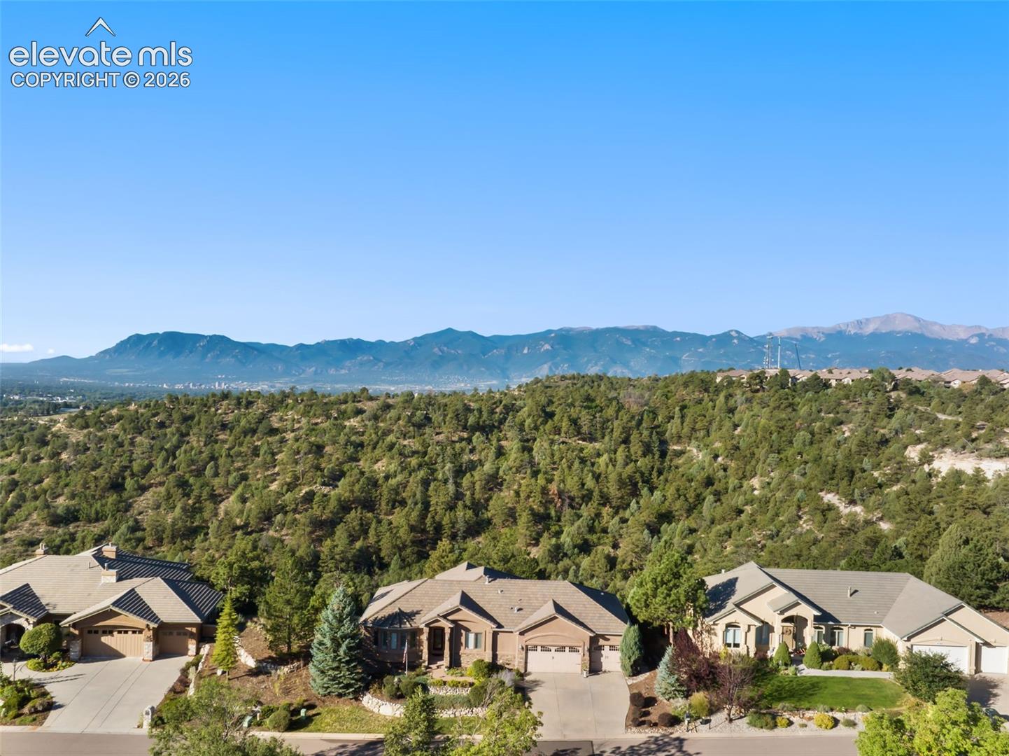 Aerial perspective of residential properties featuring stone and stucco exteriors, multi-gabled rooflines, paved driveways, and expansive mountain backdrops