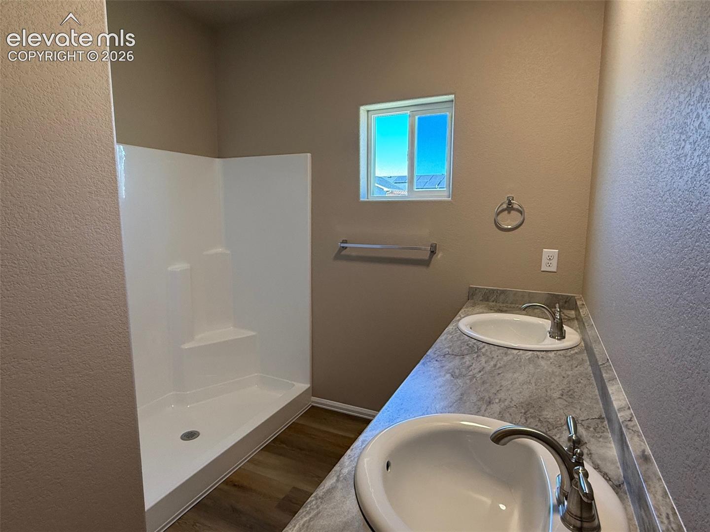 Dual vanity with integrated sinks, brushed nickel fixtures, wood-finish flooring, and a white shower stall with built-in shelving