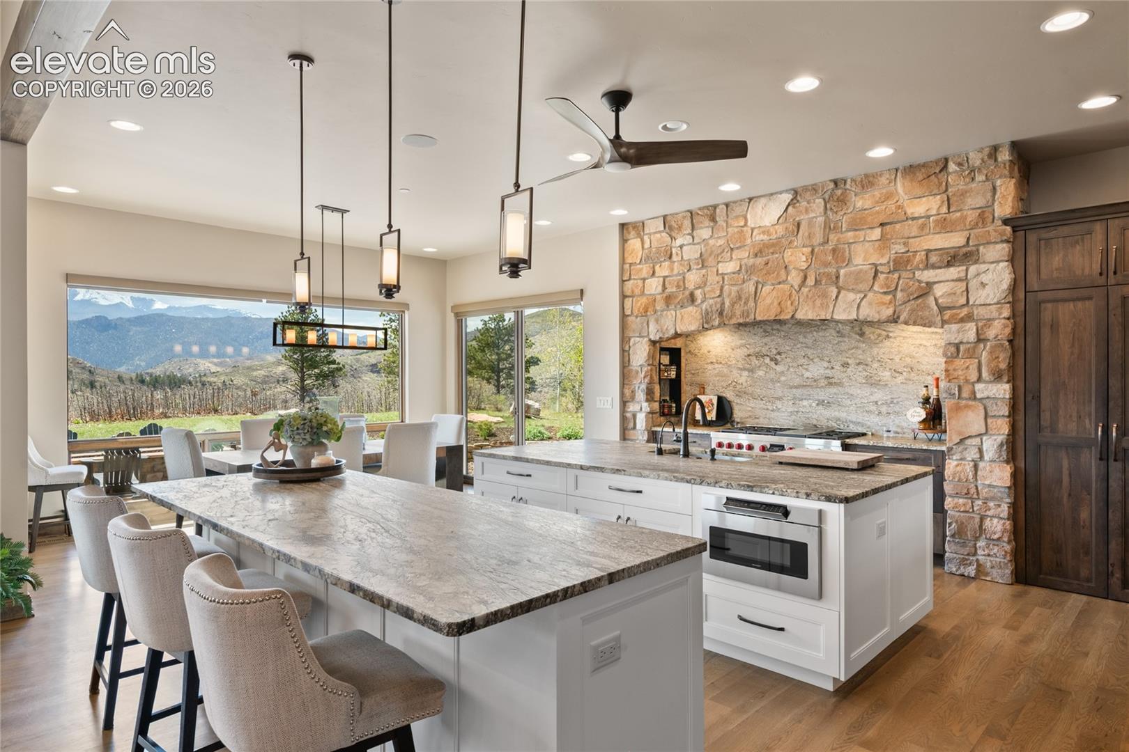Spacious entertaining kitchen with dual leathered granite islands, custom pendant lighting, walk-out access, and uninterrupted mountain views.

