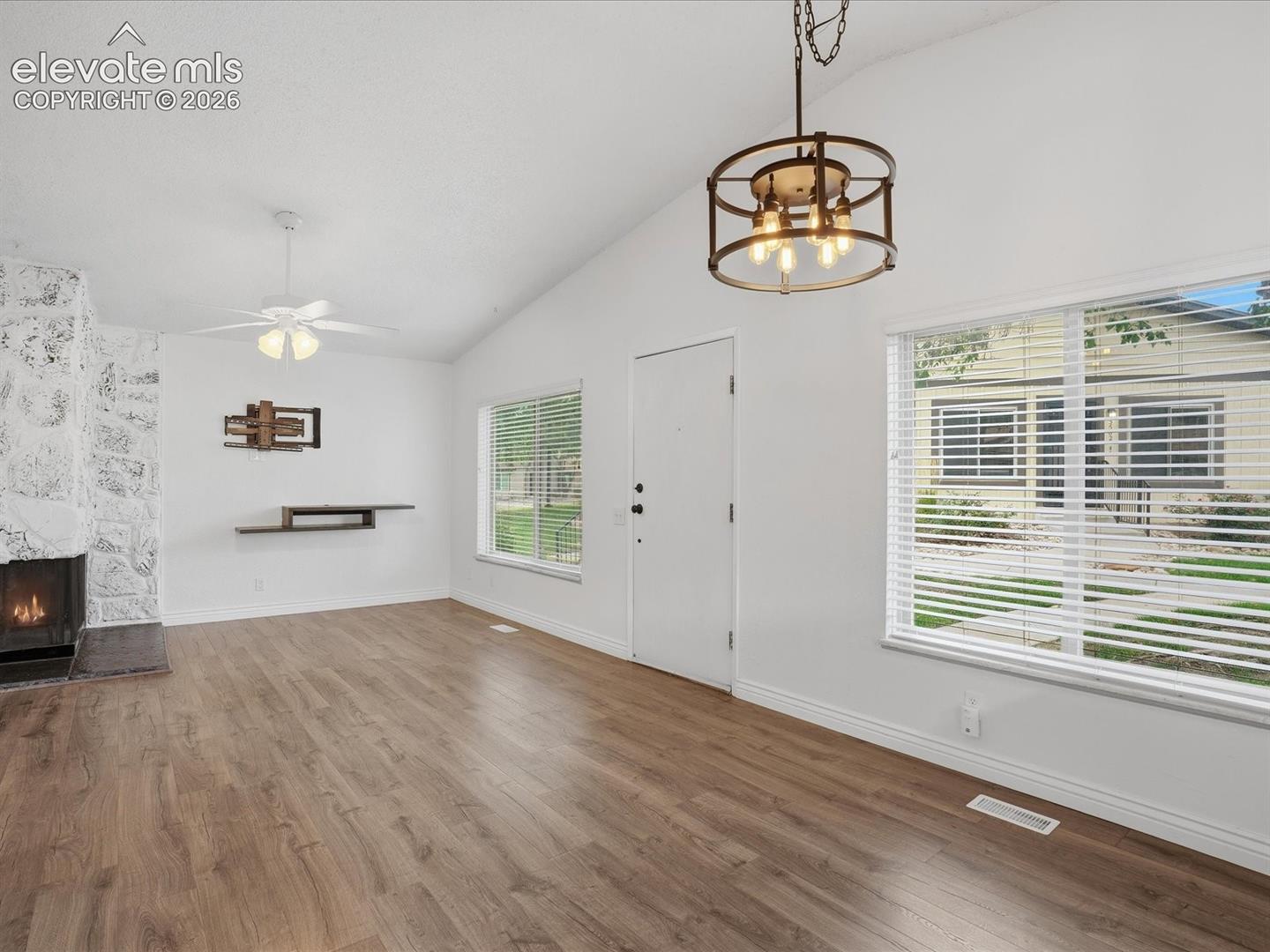 Vaulted ceilings with a geometric metal-frame chandelier, wood-finish flooring, and a stone-clad fireplace hearth