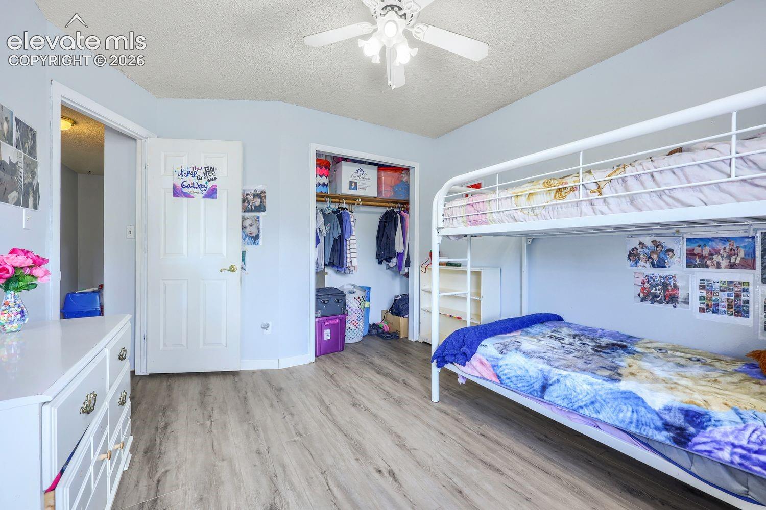Wood-finish flooring throughout, ceiling fan with light fixture, and an open closet with built-in shelving