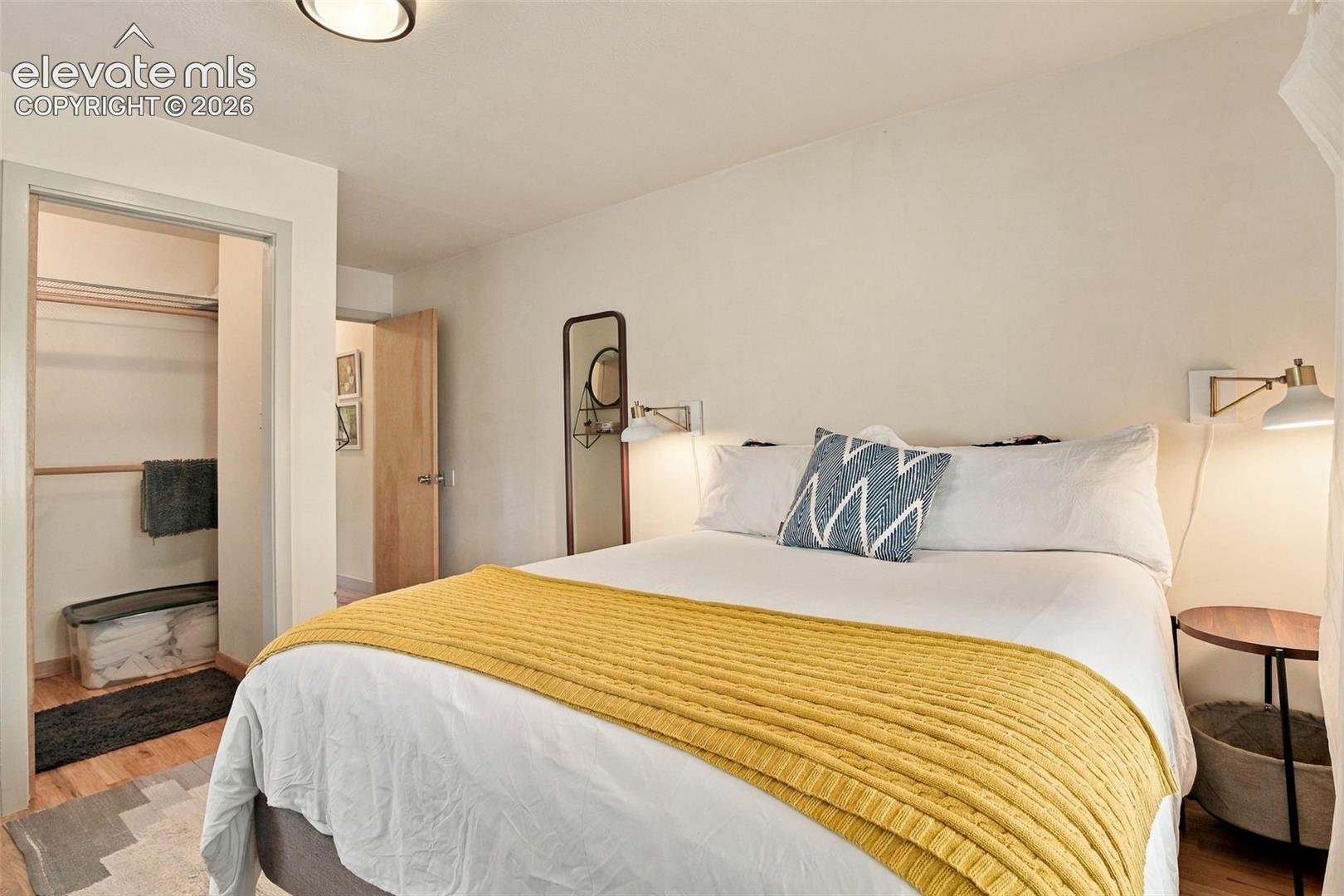 Room featuring wood-finish flooring, a walk-in closet with built-in shelving, two wall-mounted adjustable sconce lights, and a flush-mount ceiling light fixture