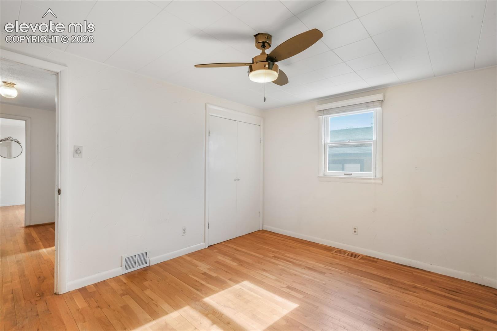 Hardwood flooring, white walls, white ceiling, ceiling fan with integrated light, and a window with blinds