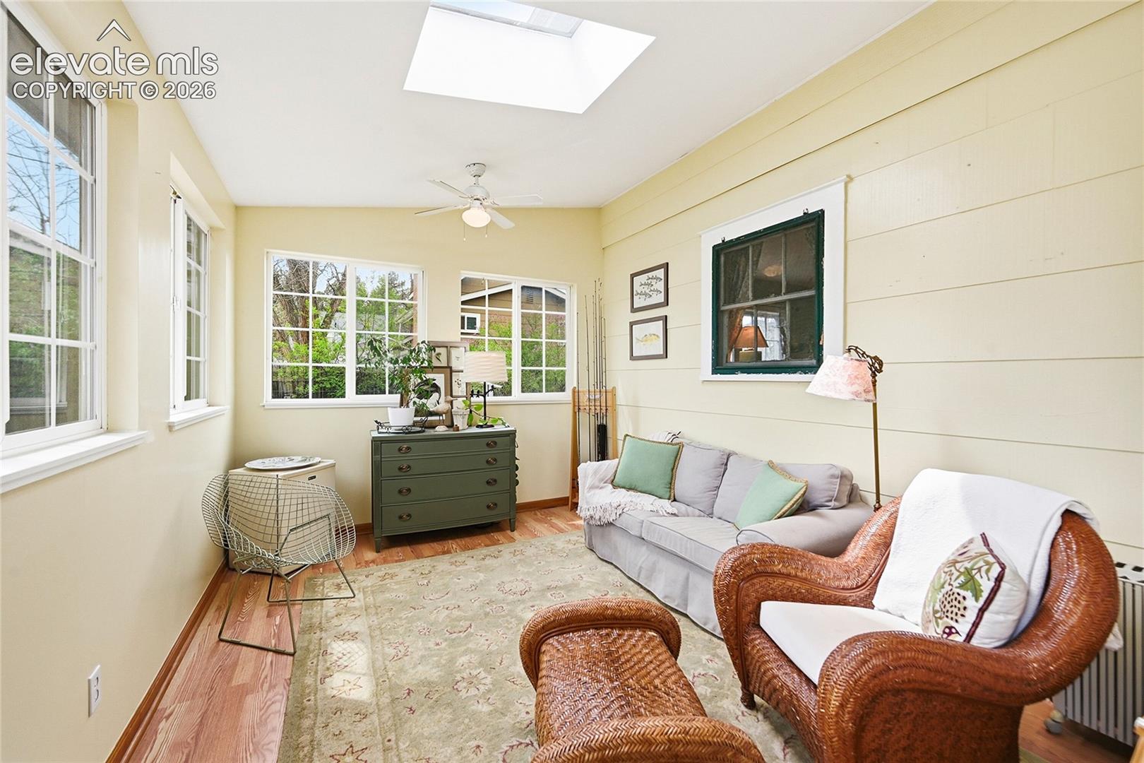 Sunroom featuring wood-finish flooring, a skylight, horizontal paneled walls, and multiple grid-pattern windows