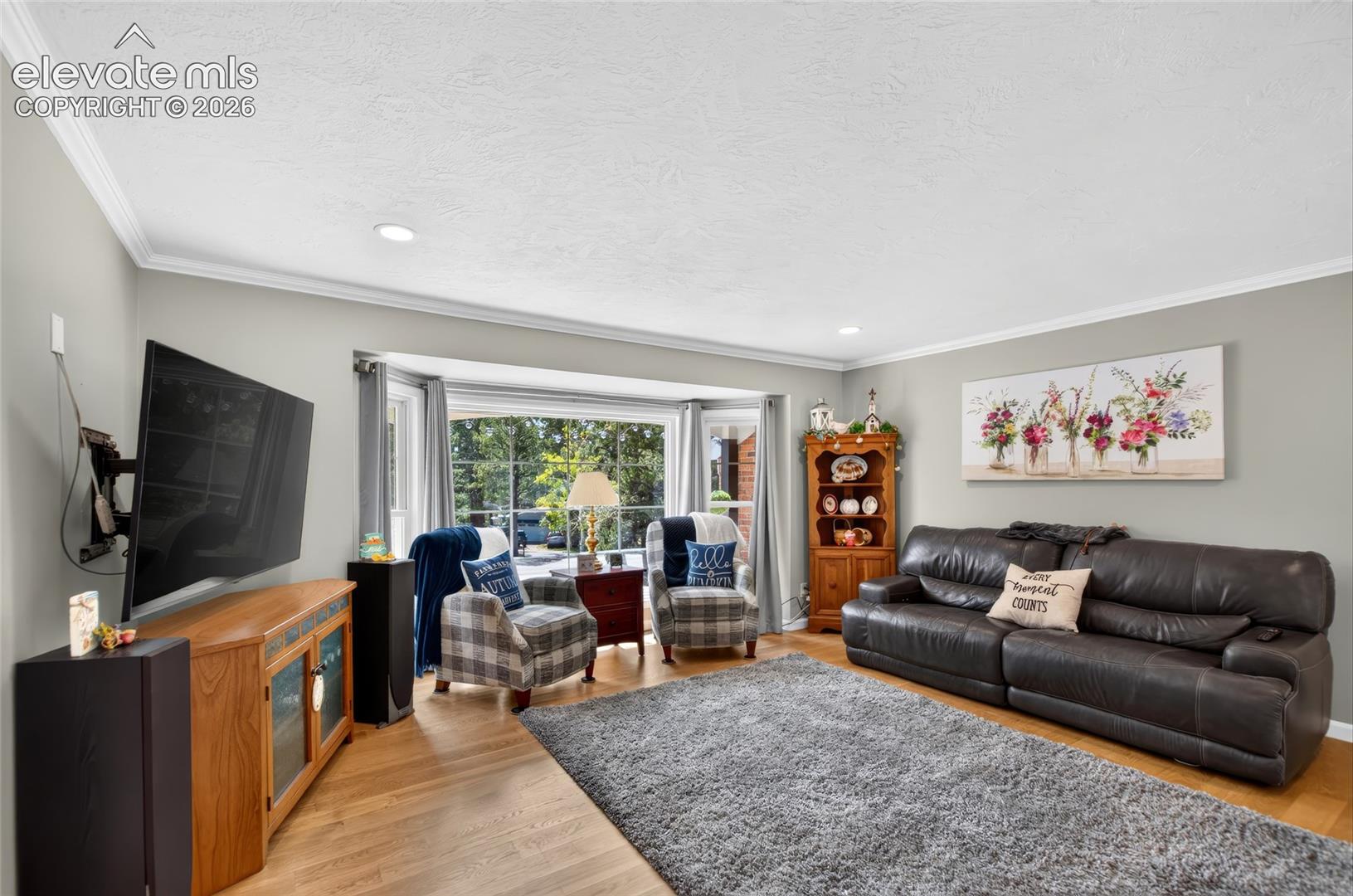Hardwood flooring, recessed ceiling lighting, crown molding, bay window, and light gray wall paint