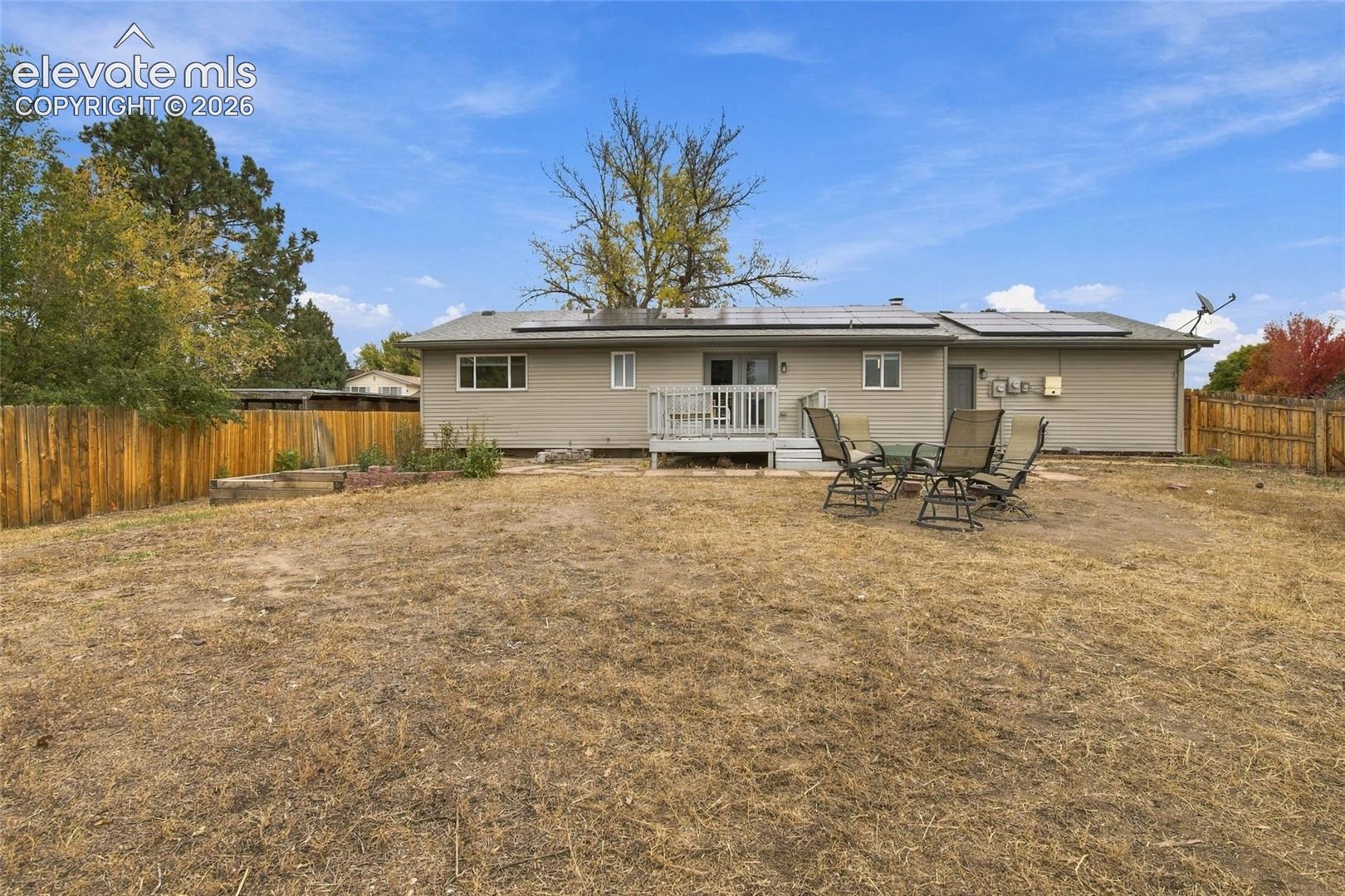 Expansive backyard featuring wood-plank fencing, solar roof panels, and an elevated wood deck