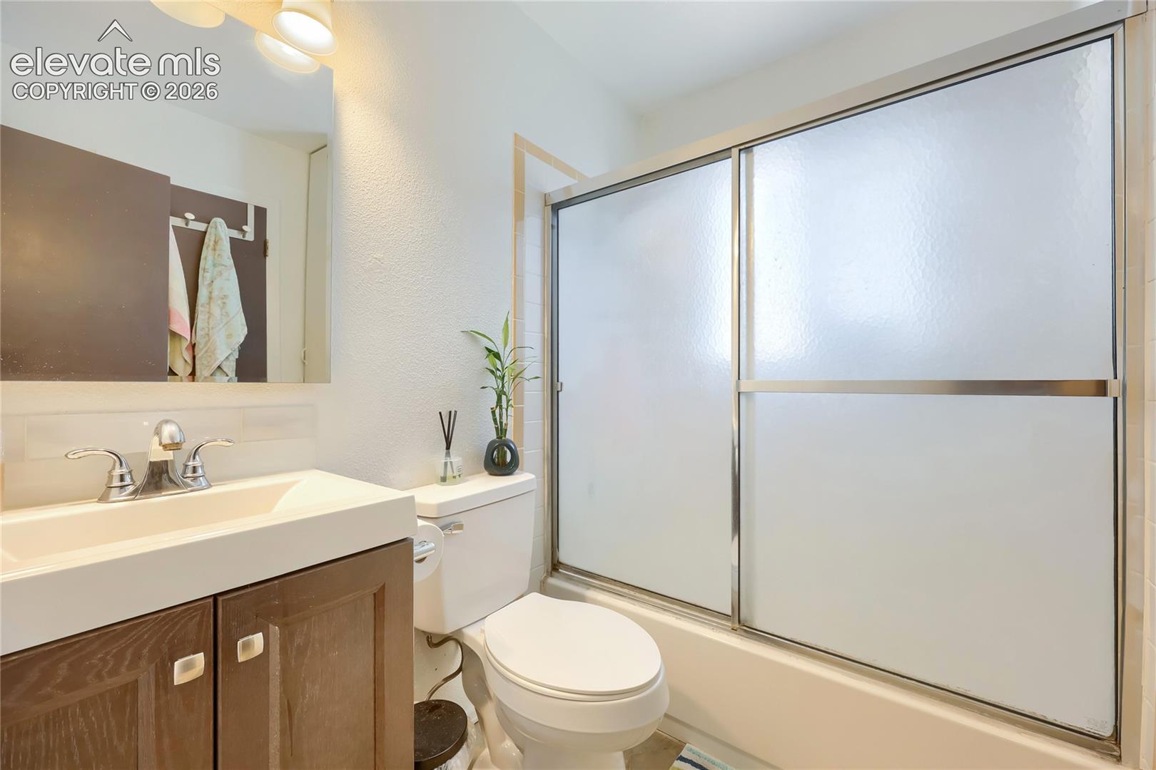 Bathroom featuring a wood-finish vanity with a rectangular sink, brushed-metal faucet, wall-mounted mirror, and a tub-shower combination with sliding frosted-glass doors