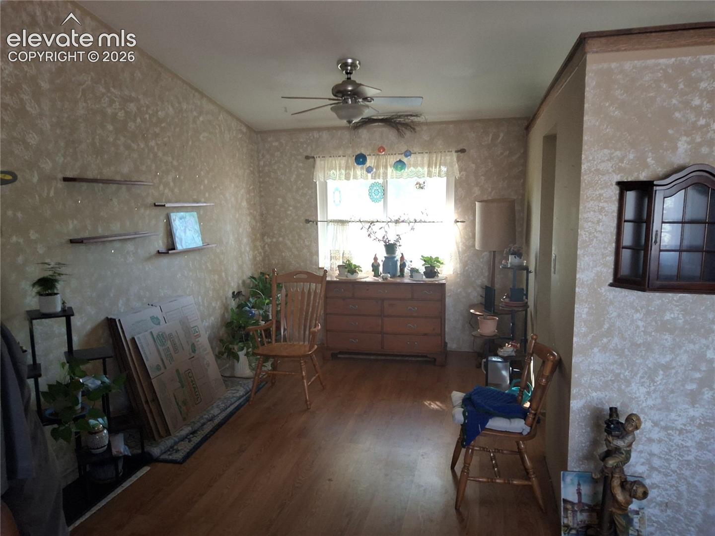 Room featuring wood-finish flooring, textured wall finishes, a central ceiling fan, wall-mounted shelving, and a wood-toned built-in wall cabinet