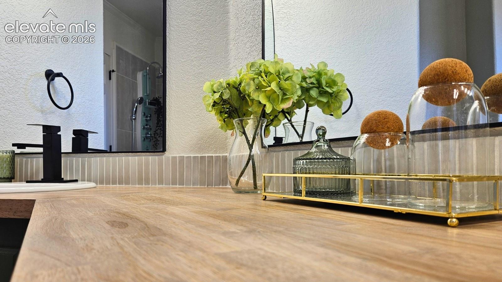 Bathroom vanity featuring a wood-finish countertop, vertical tile backsplash, dual black-framed mirrors, matte black fixtures, and circular wall-mounted towel ring