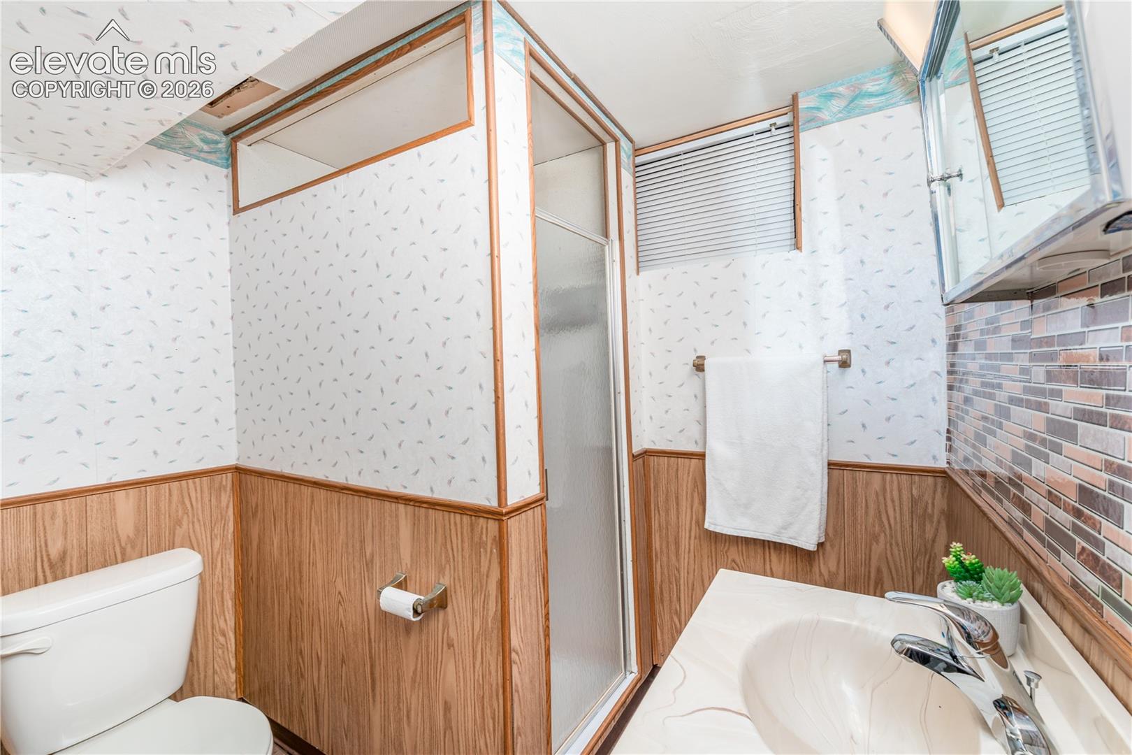 Bathroom featuring a shower enclosure with a frosted panel, a toilet, a vanity with an integrated sink, a mirrored medicine cabinet, and wood-finish wall paneling