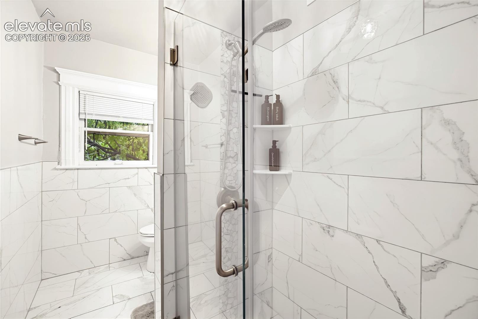 Shower enclosure with glass door, white tile walls, and integrated shower shelves