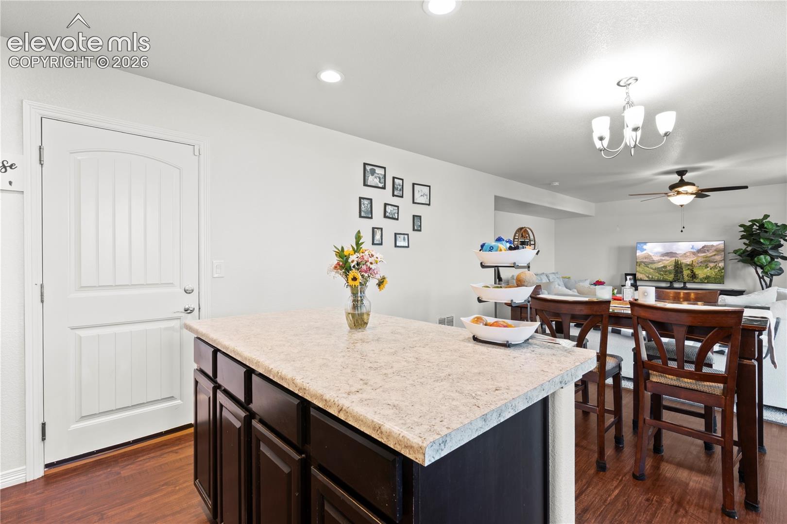 Center island with a stone-finish countertop and dark cabinetry, wood-finish flooring, recessed lighting, and a multi-light chandelier