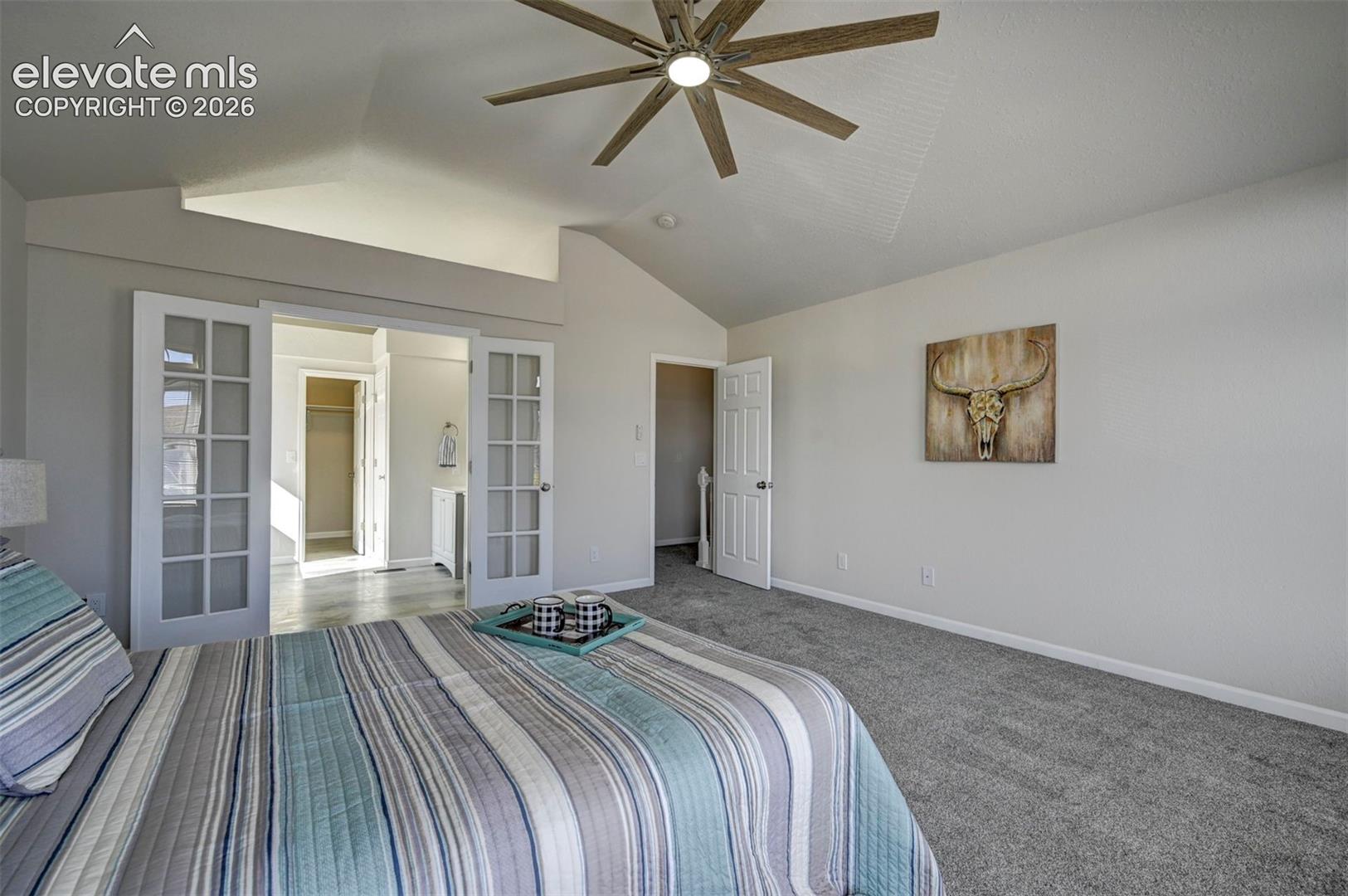 Vaulted ceilings featuring a multi-blade ceiling fan, neutral wall tones, and glass-paned double doors