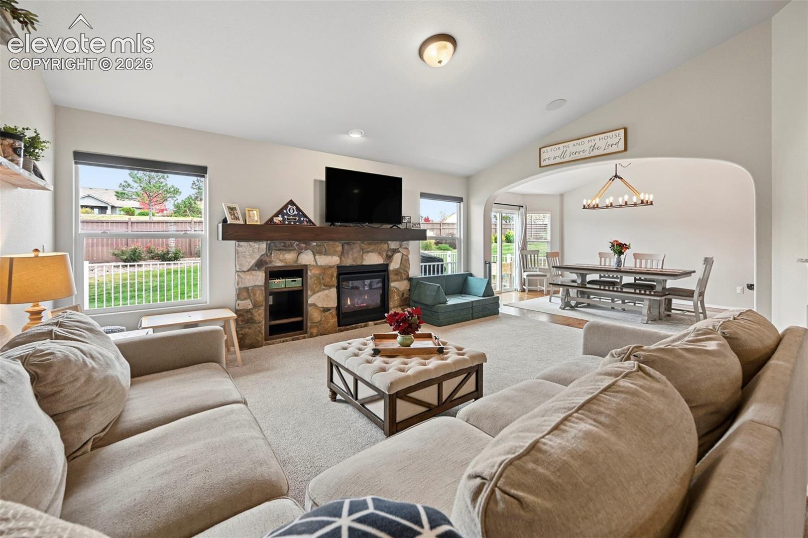 Vaulted ceilings, stone-surround fireplace with a timber mantel, built-in media storage, recessed lighting, and an arched entry