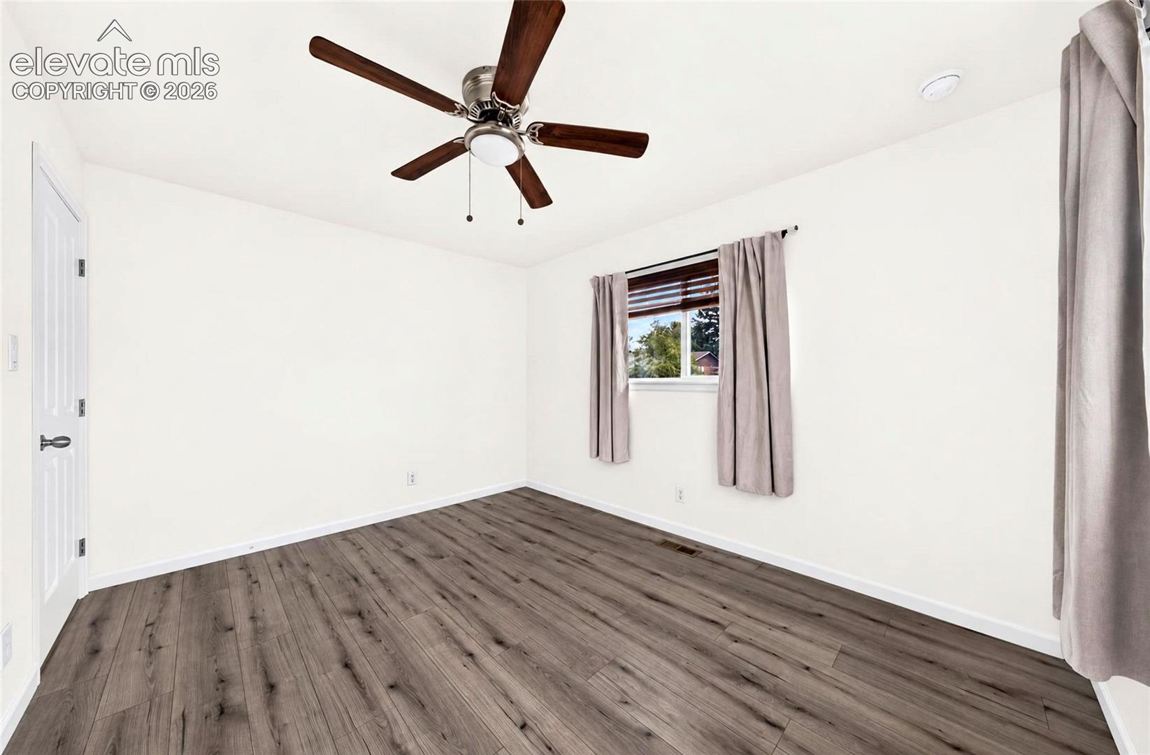 Room featuring wood-finish flooring, a ceiling fan with integrated lighting, a multi-panel door, and a horizontal window