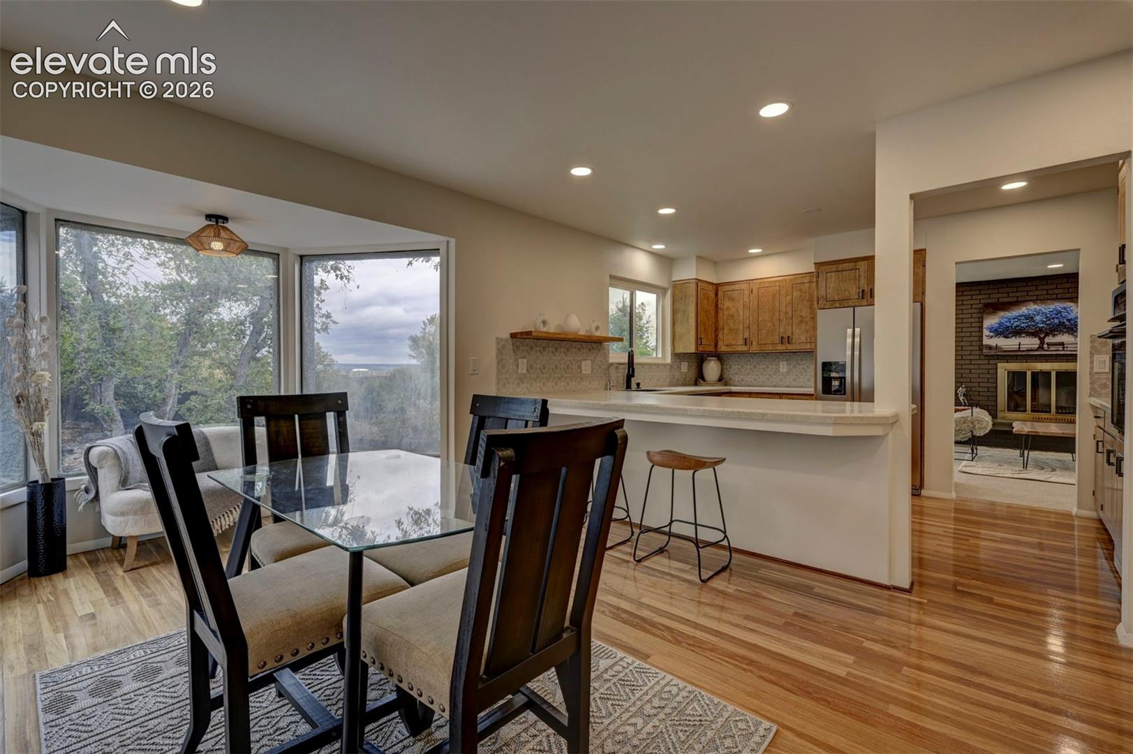 Kitchen featuring wood cabinetry, recessed lighting, a raised countertop breakfast bar, and wood-finish flooring, incorporating a dining area with a bay window