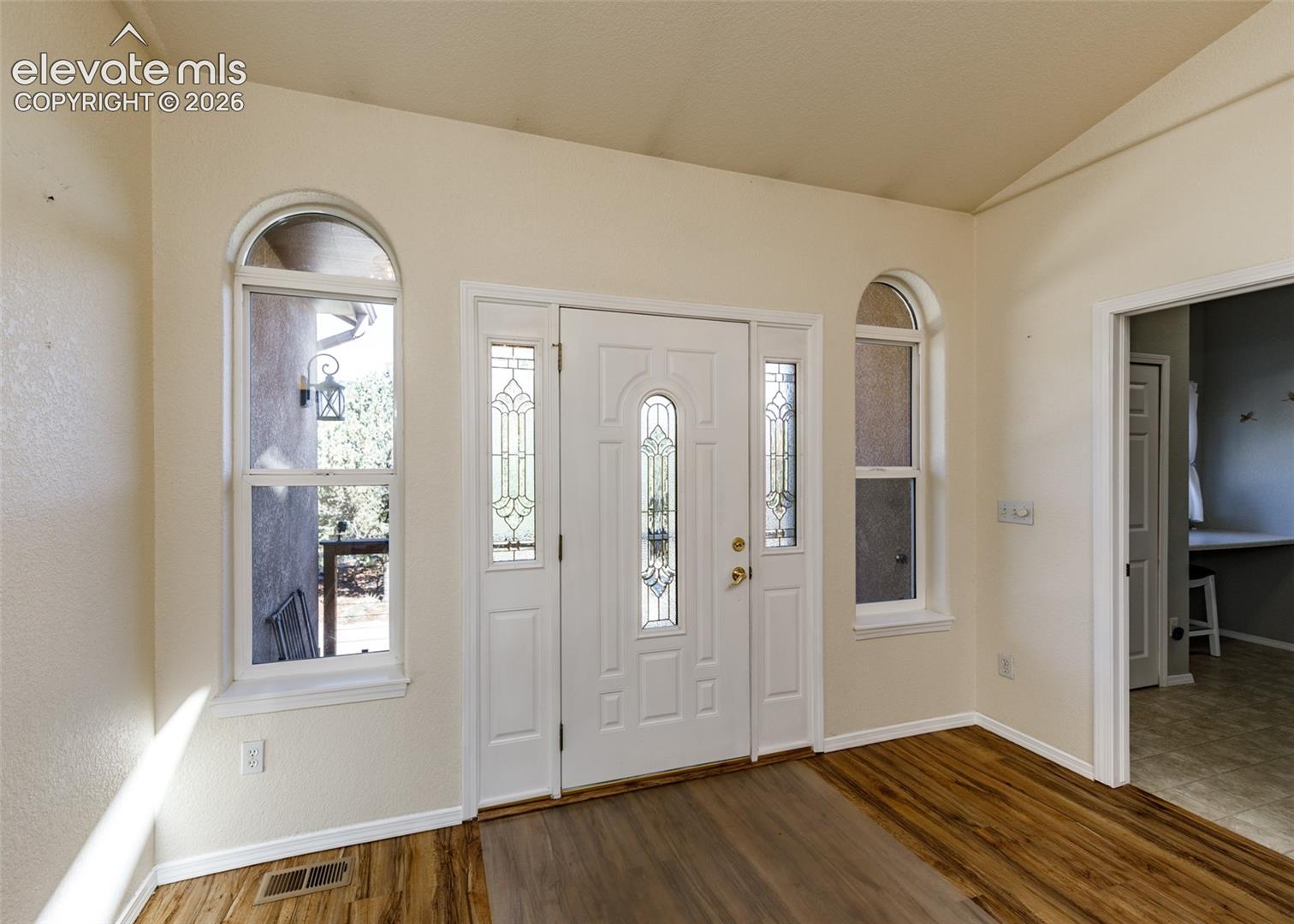Entryway featuring wood-finish flooring, vaulted ceilings, and a paneled front door with decorative leaded glass inserts flanked by sidelights and arched windows