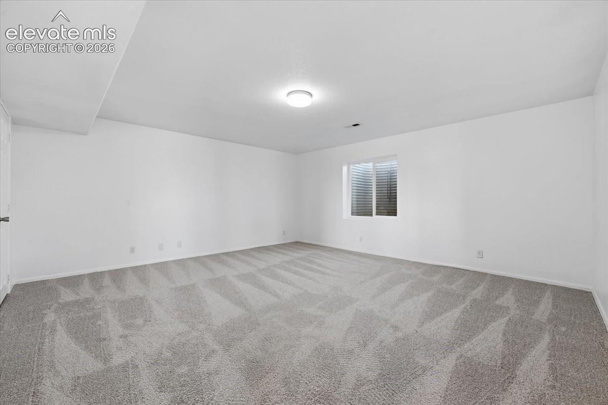Neutral-toned interior space featuring wall-to-wall carpeting, crisp white wall finishes, and a flush-mount ceiling light fixture
