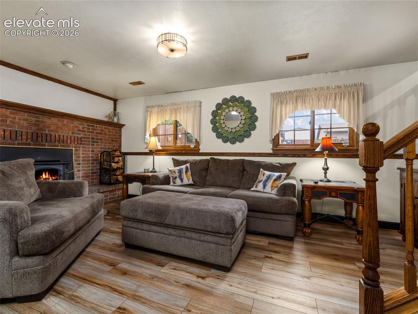Brick fireplace with wood-burning stove, wood-finish flooring, and wood-trimmed windows