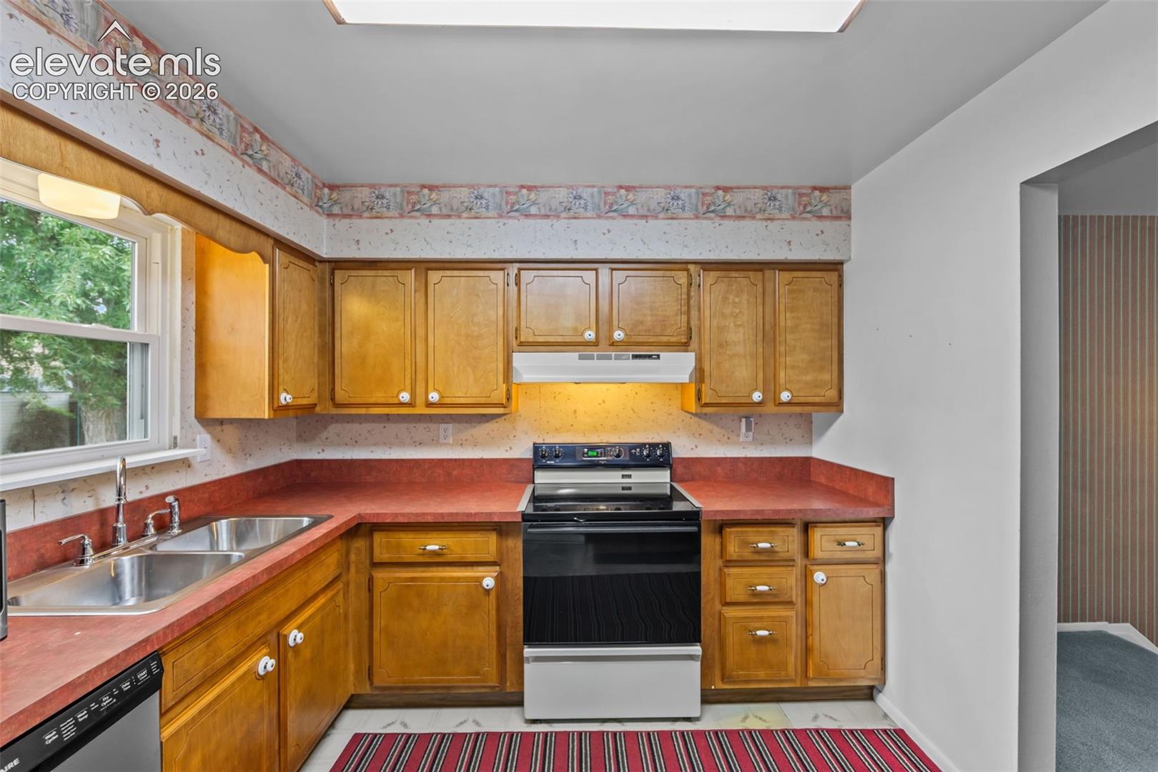 Kitchen featuring wood cabinetry, red countertops, a double basin sink, and a built-in electric range with overhead ventilation