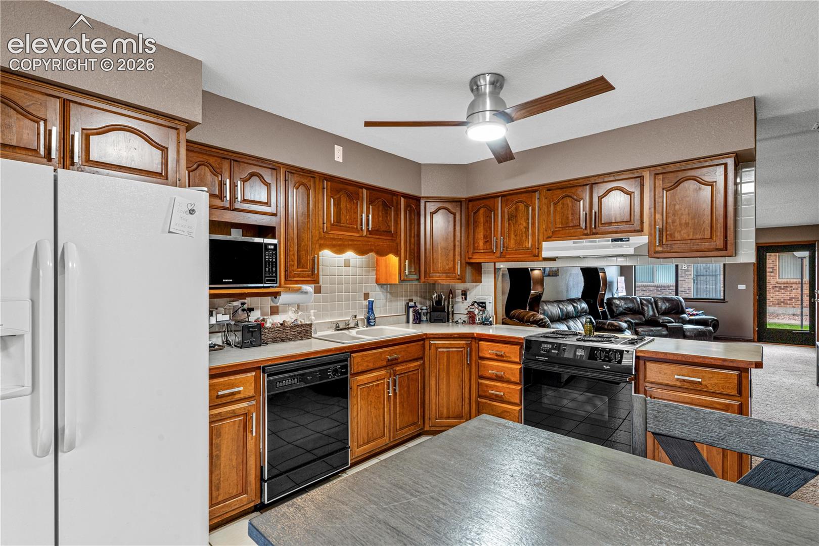 Kitchen featuring warm-tone wood cabinetry, tiled backsplash, integrated appliance suite, and a ceiling-mounted light fixture