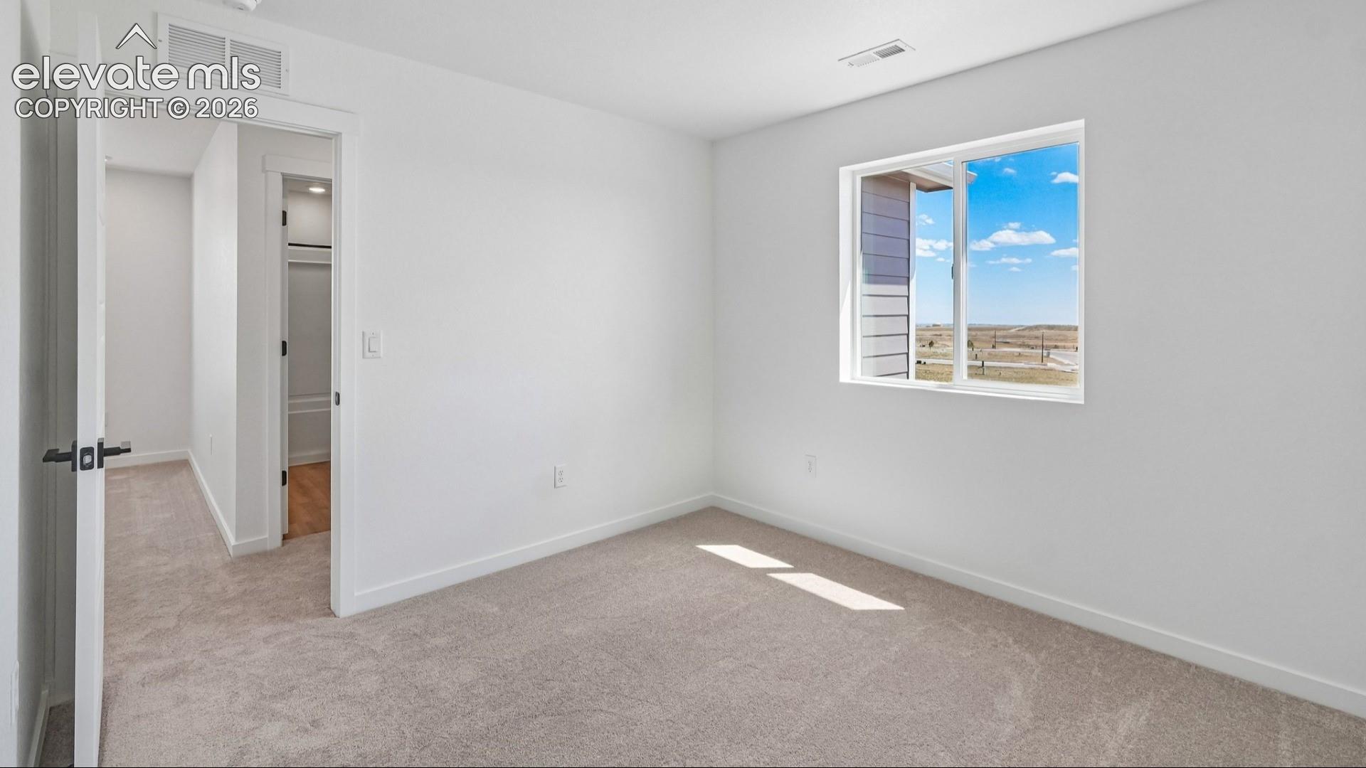 Neutral-toned wall-to-wall carpeting, window with exterior landscape imagery, and interior doors with matte black hardware