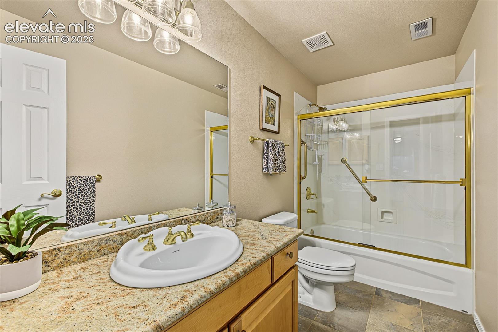 Full bathroom located between two additional bedrooms in the full walkout basement, featuring a granite-topped vanity, tub and shower combination with glass enclosure, and tile flooring.