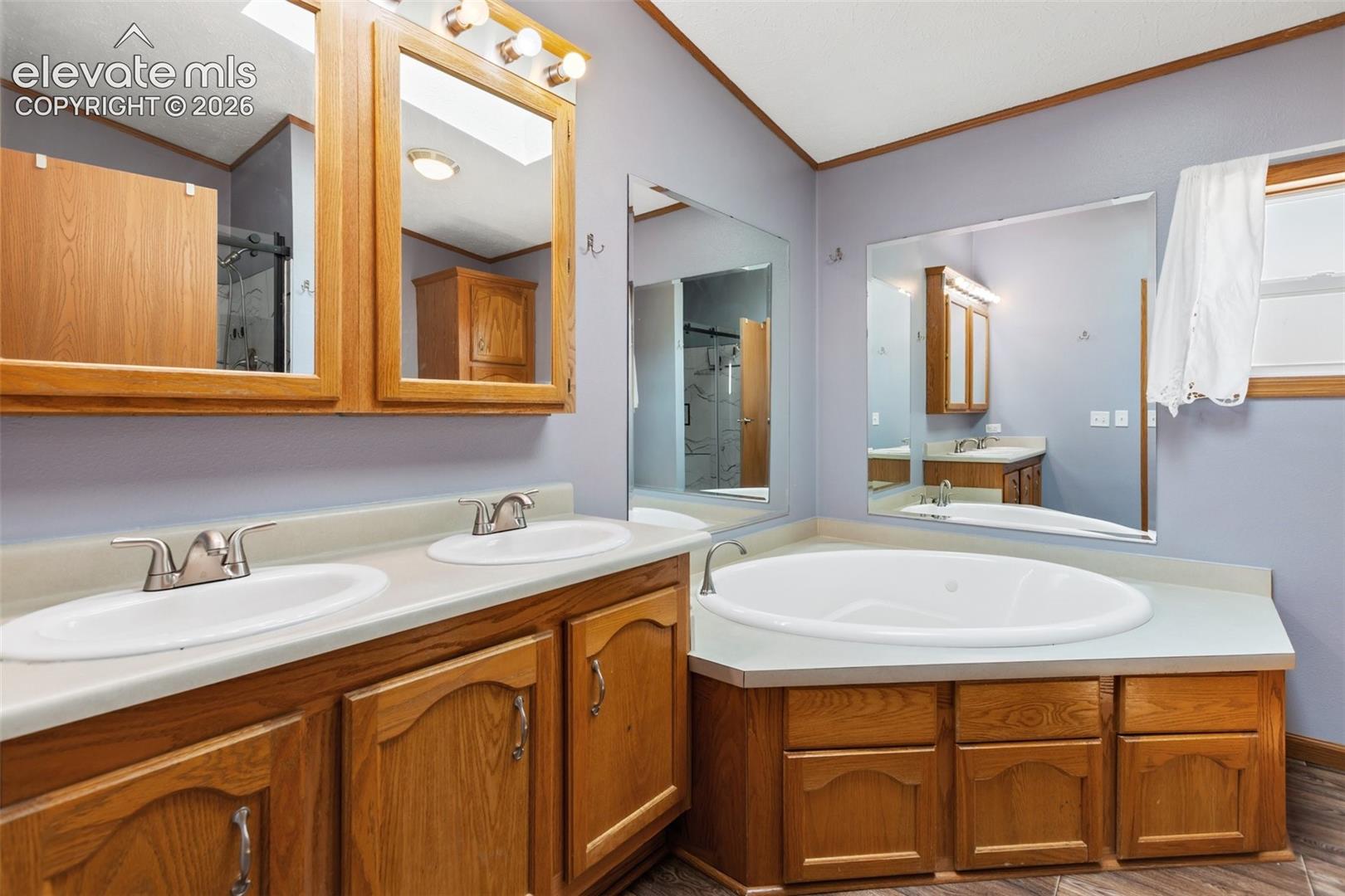 Spacious bathroom featuring a built-in corner soaking tub, a dual vanity with light-toned countertops, and wood-finish cabinetry