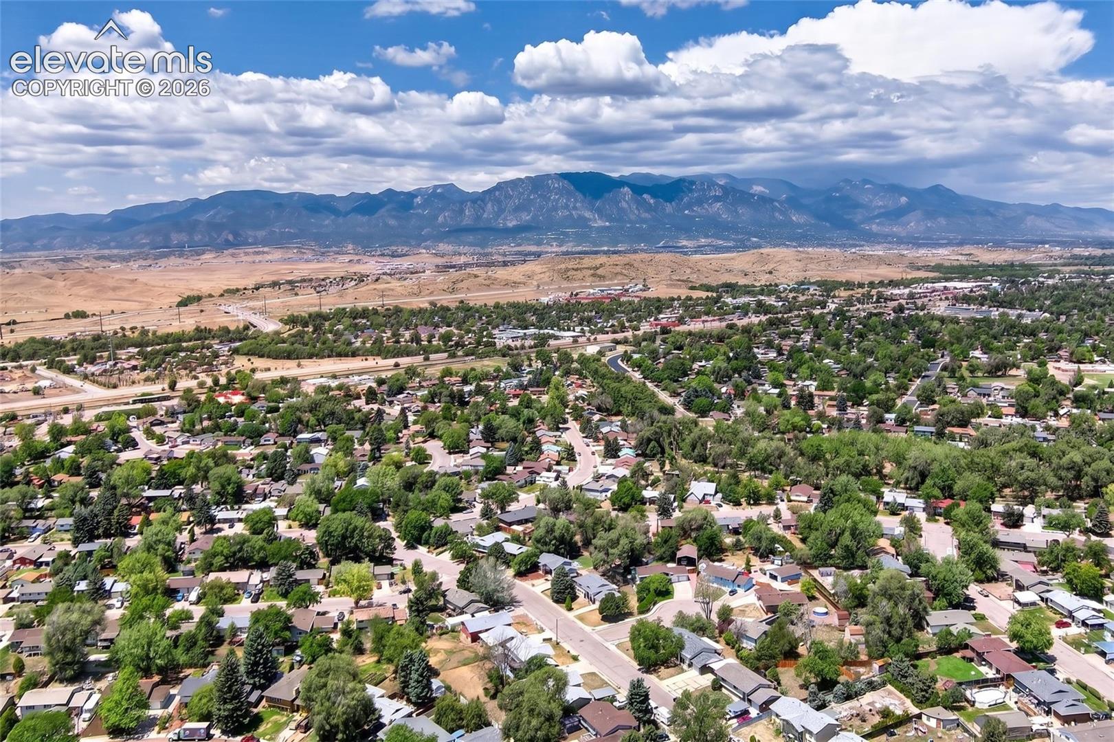 Expansive residential area featuring established homes, mature trees, paved streets, and mountainous terrain in the distance