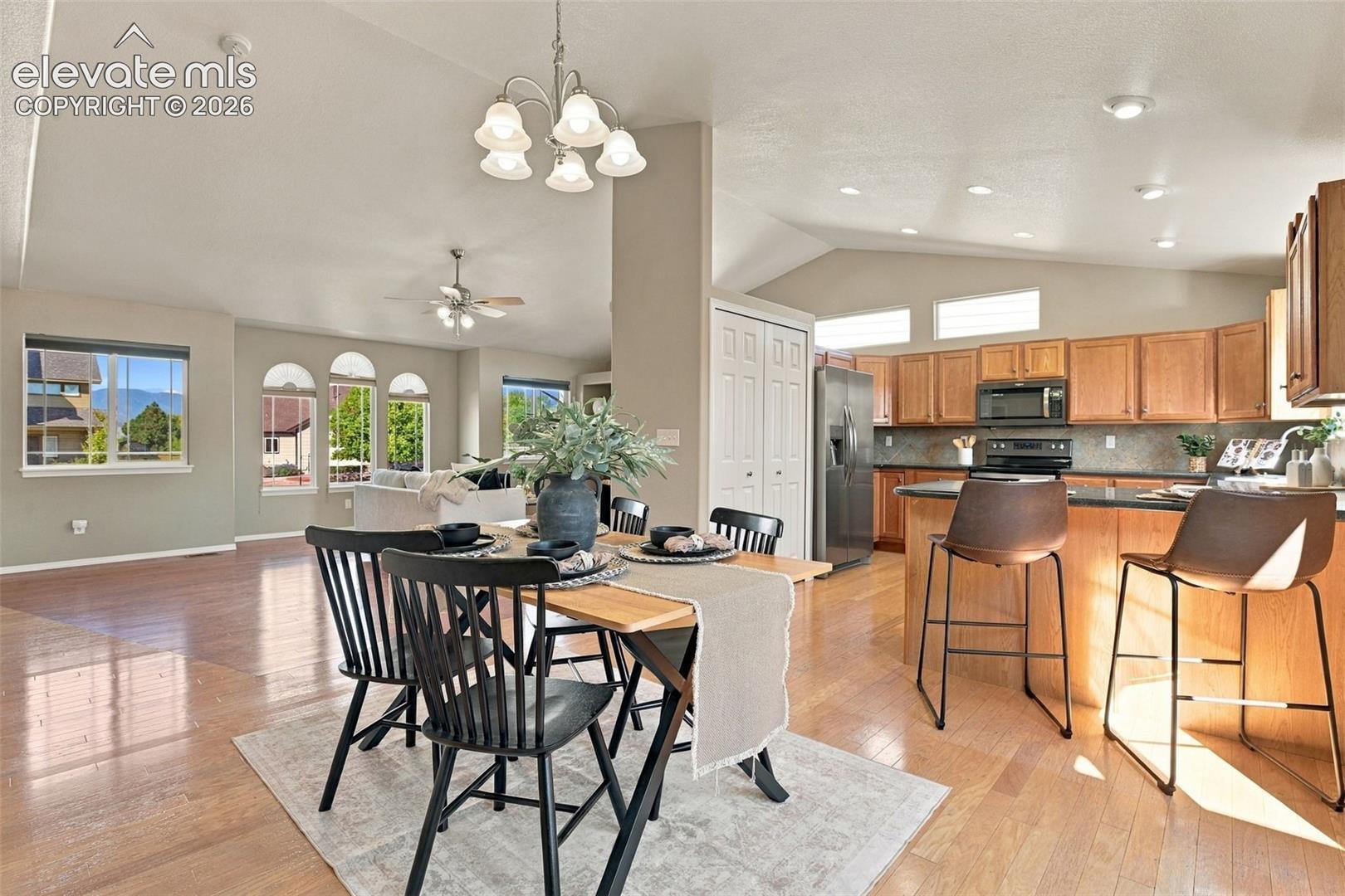 Wood-finish flooring throughout, vaulted ceilings, kitchen with wood cabinetry and dark countertops, stainless steel appliances, and abundant natural light from multiple windows