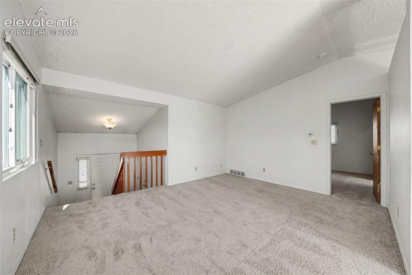 Vaulted ceilings, neutral carpeting, and a wooden handrail overlooking the entry area
