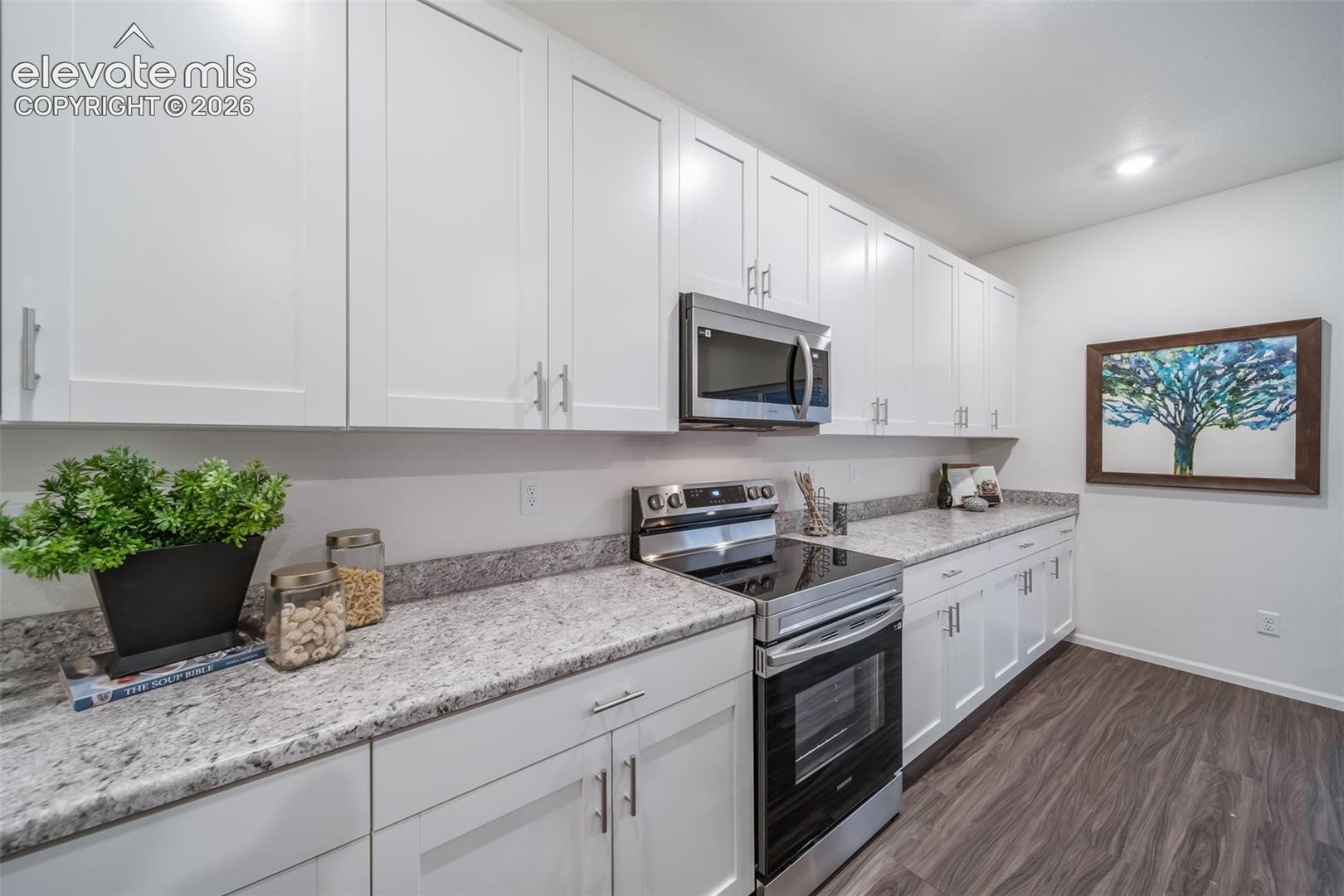 White shaker-style cabinetry, stainless steel oven with an electric cooktop, stainless steel microwave, speckled stone-finish countertops, and wood-finish flooring
*photos of a model home*