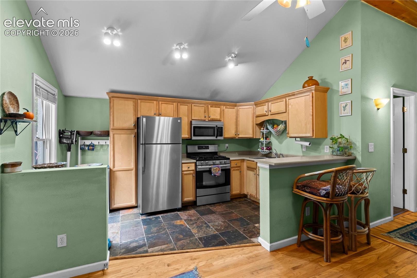 Kitchen featuring vaulted ceilings, slate tile flooring, natural wood cabinetry, stainless steel appliances, and a breakfast bar
