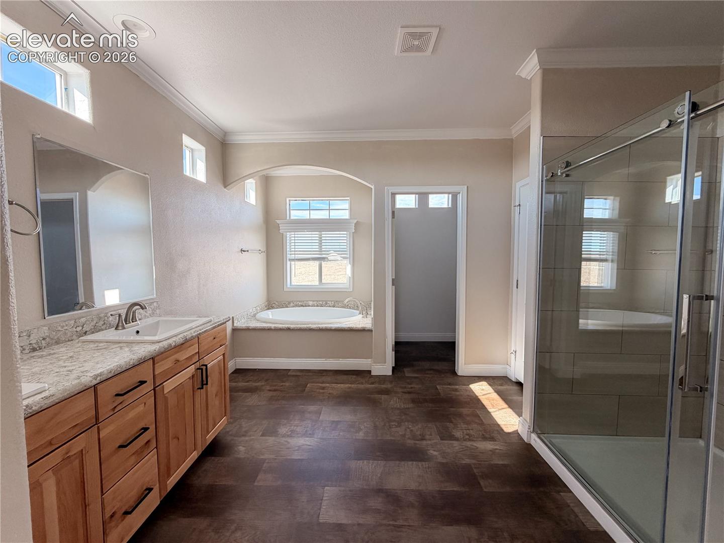 Bathroom featuring a wood-finish vanity with a stone countertop, an integrated drop-in soaking tub with a stone deck, a tiled glass-enclosed shower, and tile flooring