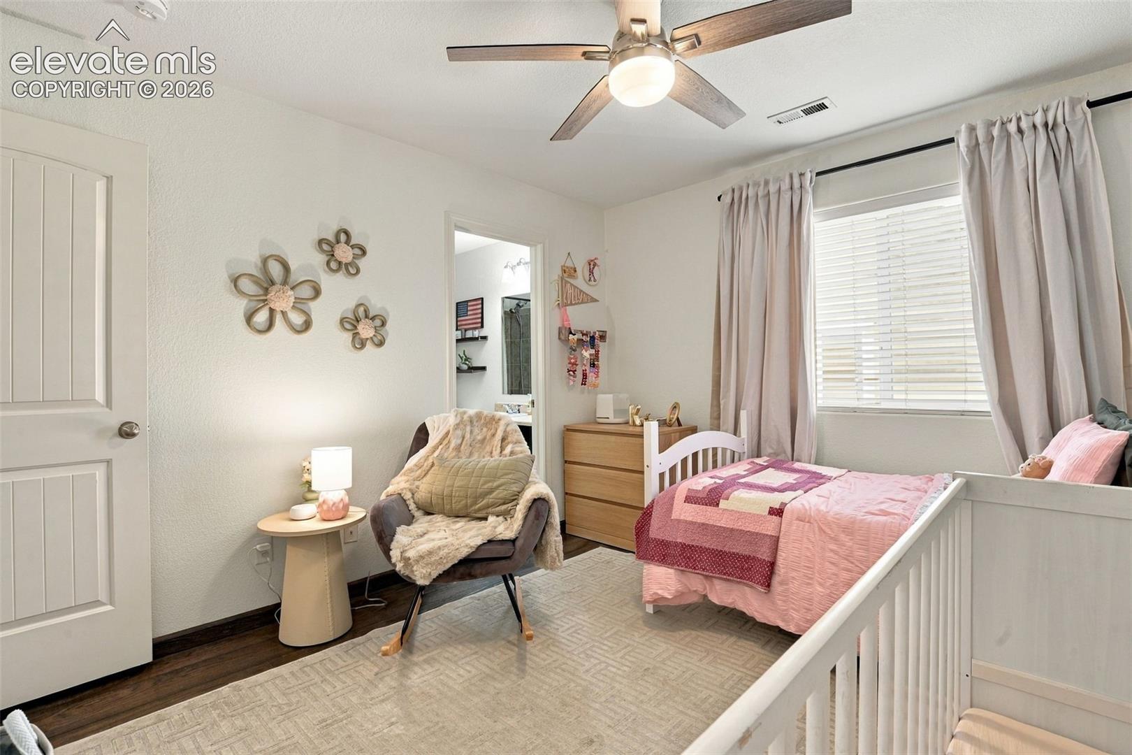 Wood-finish flooring, white paneled door, ceiling fan with integrated lighting, window with blinds and drapes, and a built-in dresser