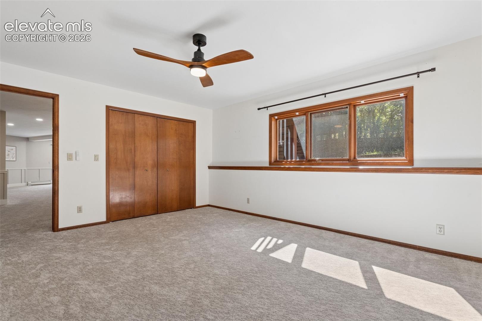 Carpeted room with a ceiling fan, wood-framed window, and wood bifold closet doors