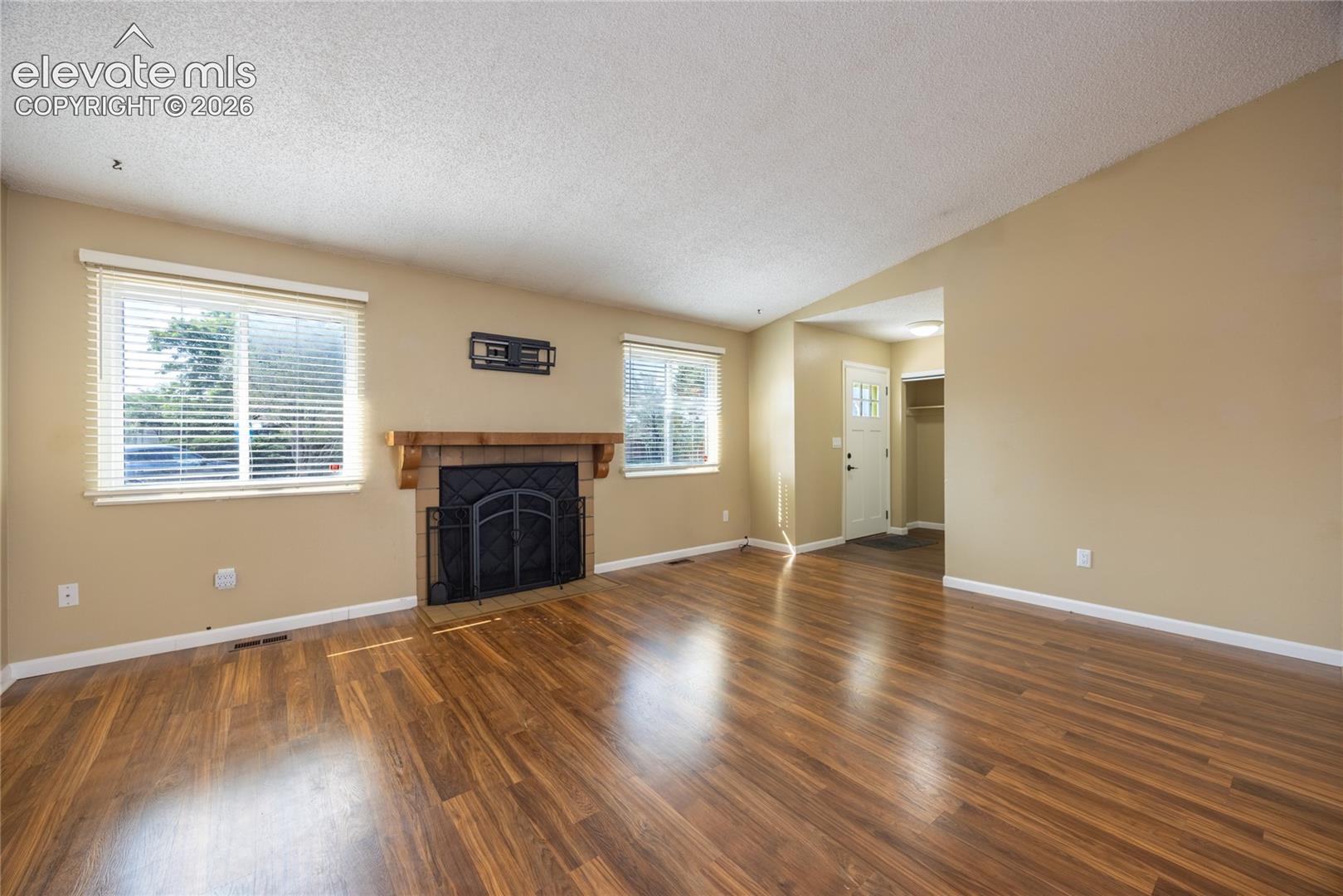 Wood-finish flooring throughout, framed windows with blinds, and a fireplace with a brick surround and wood mantel