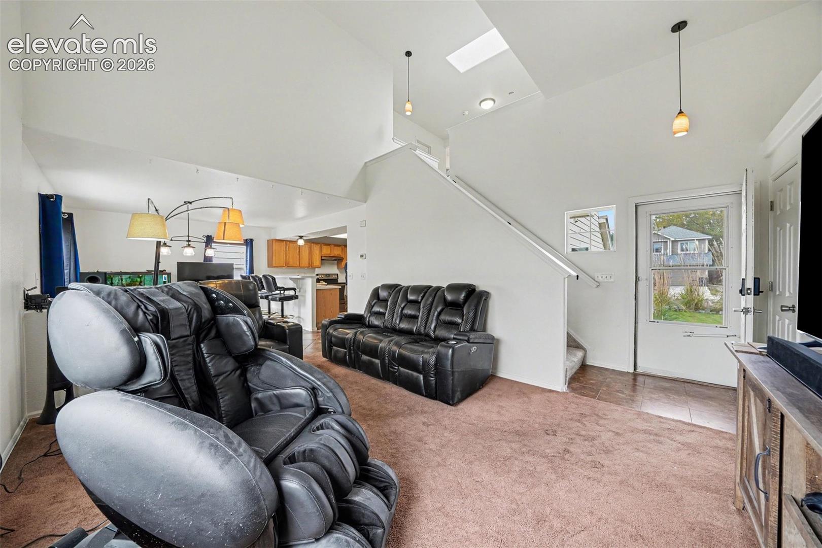 Vaulted ceiling featuring a skylight, pendant lighting, carpeted flooring, and a staircase with a handrail