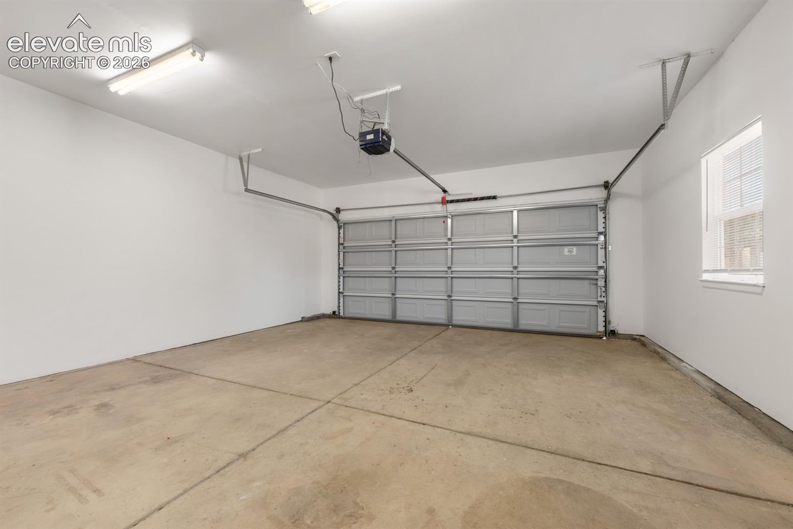 Garage space featuring painted walls, concrete flooring, a sectional garage door, a window, and overhead fluorescent lighting
