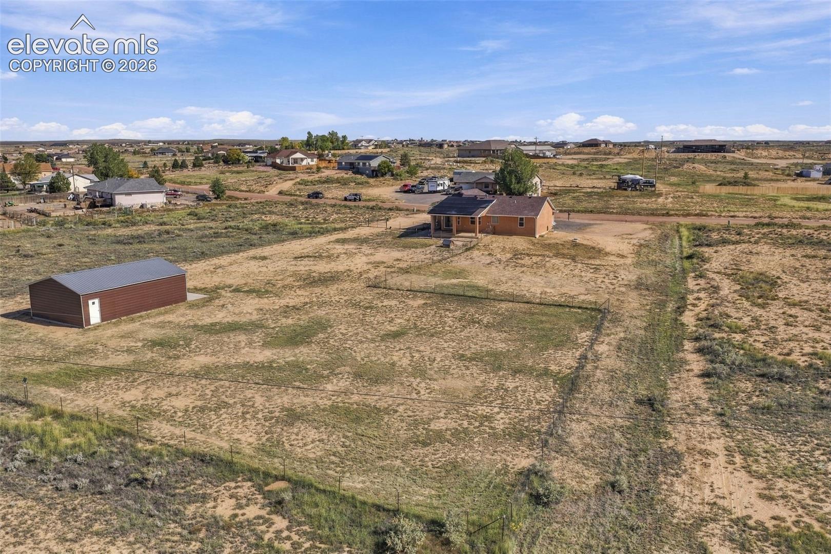 Aerial perspective featuring a detached metal structure, fenced perimeter, and expansive acreage