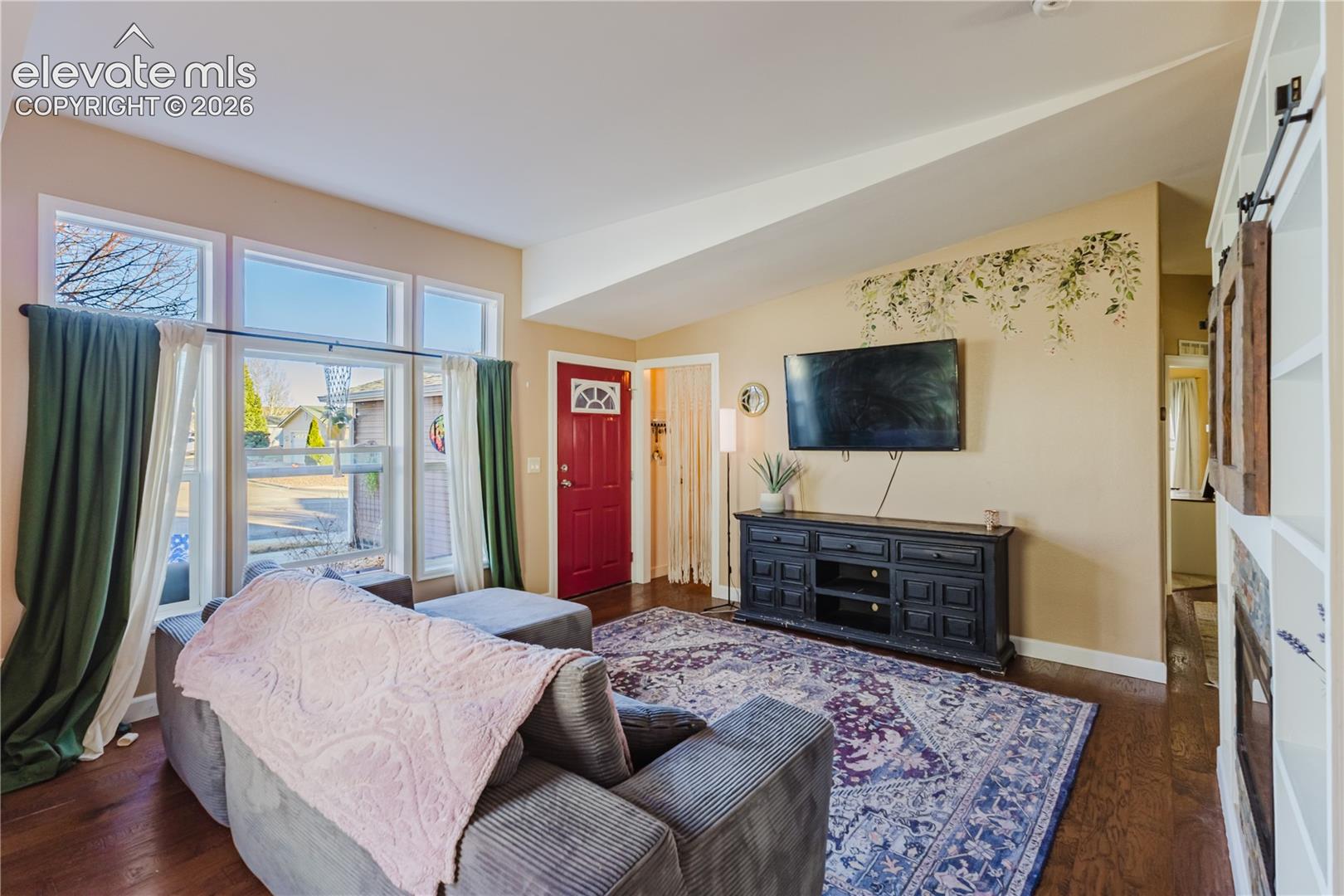 Warm wood-finish flooring, a vibrant red entry door, built-in shelving, and transom windows