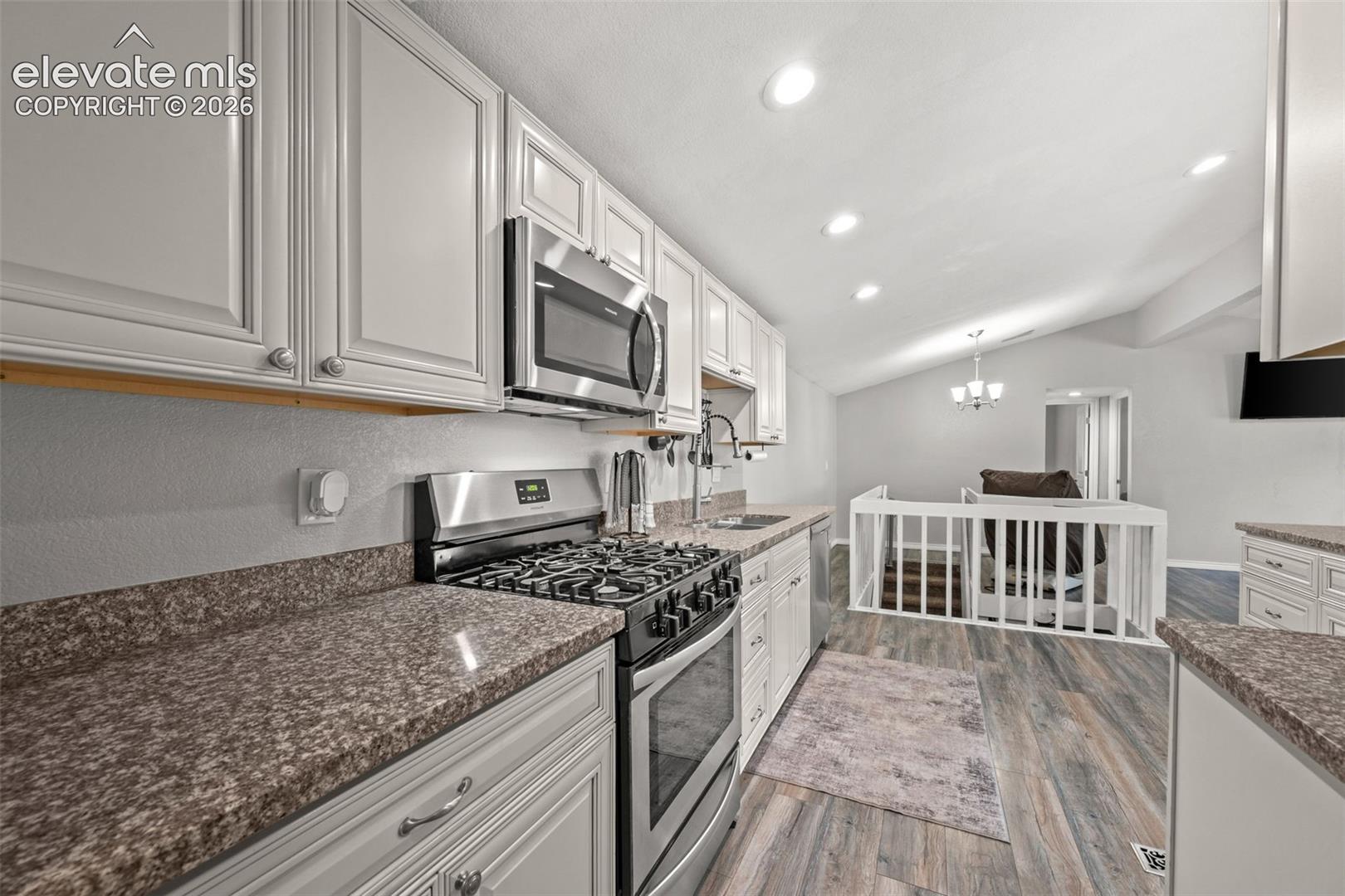 Kitchen featuring off-white cabinetry, stone-finish countertops, stainless steel gas range, built-in microwave, and wood-finish flooring