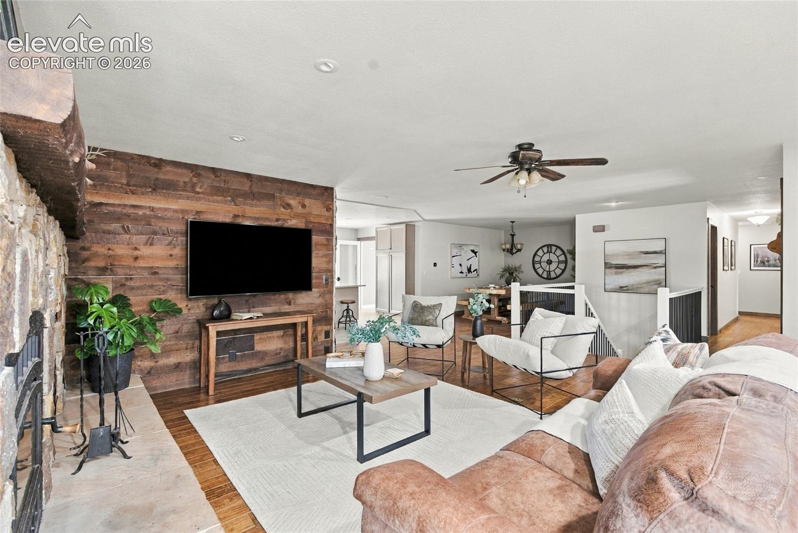 Stone fireplace with a wood mantel, wood-finish flooring, and a wood-paneled accent wall