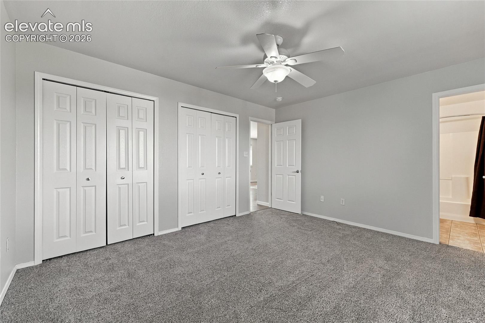Neutral-toned bedroom featuring wall-to-wall carpeting, two sets of paneled bifold closet doors, and a ceiling-mounted light fixture with integrated fan