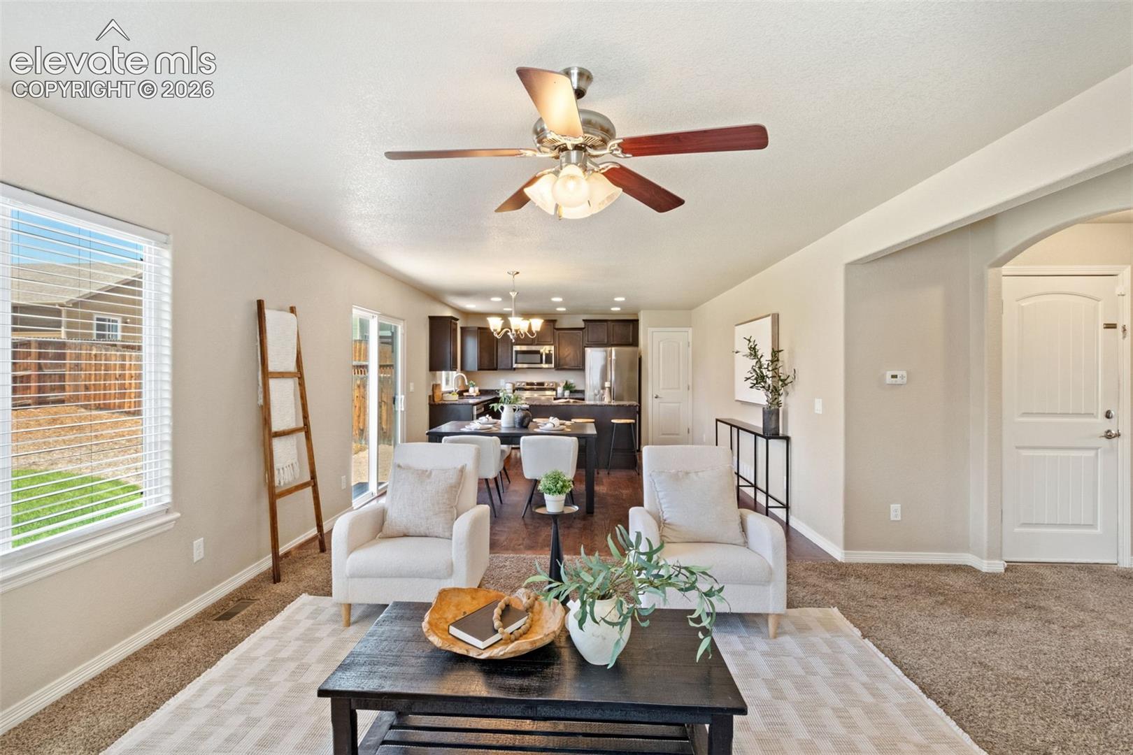 Open-concept living area featuring a ceiling fan with integrated lighting, soft neutral wall tones, and carpet flooring